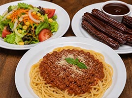 un plato de Ensalada, plato espaguetis boloñesa y Churros de chocolate